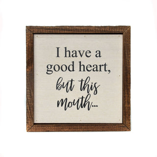 Wooden-framed sign with text 'I have a good heart, but this mouth...' on a white background