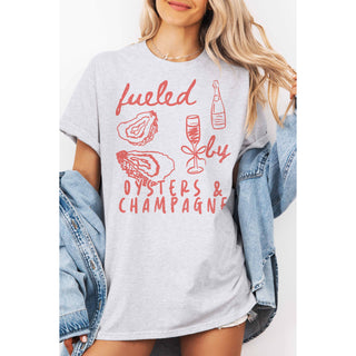 Person wearing a gray t-shirt with red graphics and text 'fueled by oysters & champagne'.