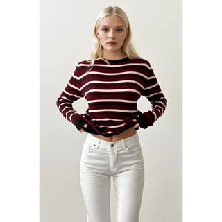 Woman wearing a striped sweater and white pants against a plain background