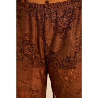 Woman wearing a brown satin outfit with lace detail asymmetric top and lace pants