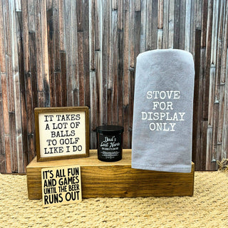 Decorative items including a towel, sign, and mug on a wooden stand against a wooden wall.