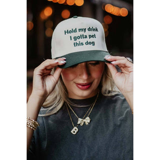 Person wearing a cap with text 'Hold my drink I gotta pet this dog' against a blurred background