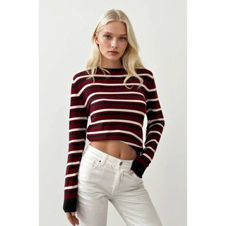 Woman wearing a maroon and white striped sweater with white pants on a light gray background